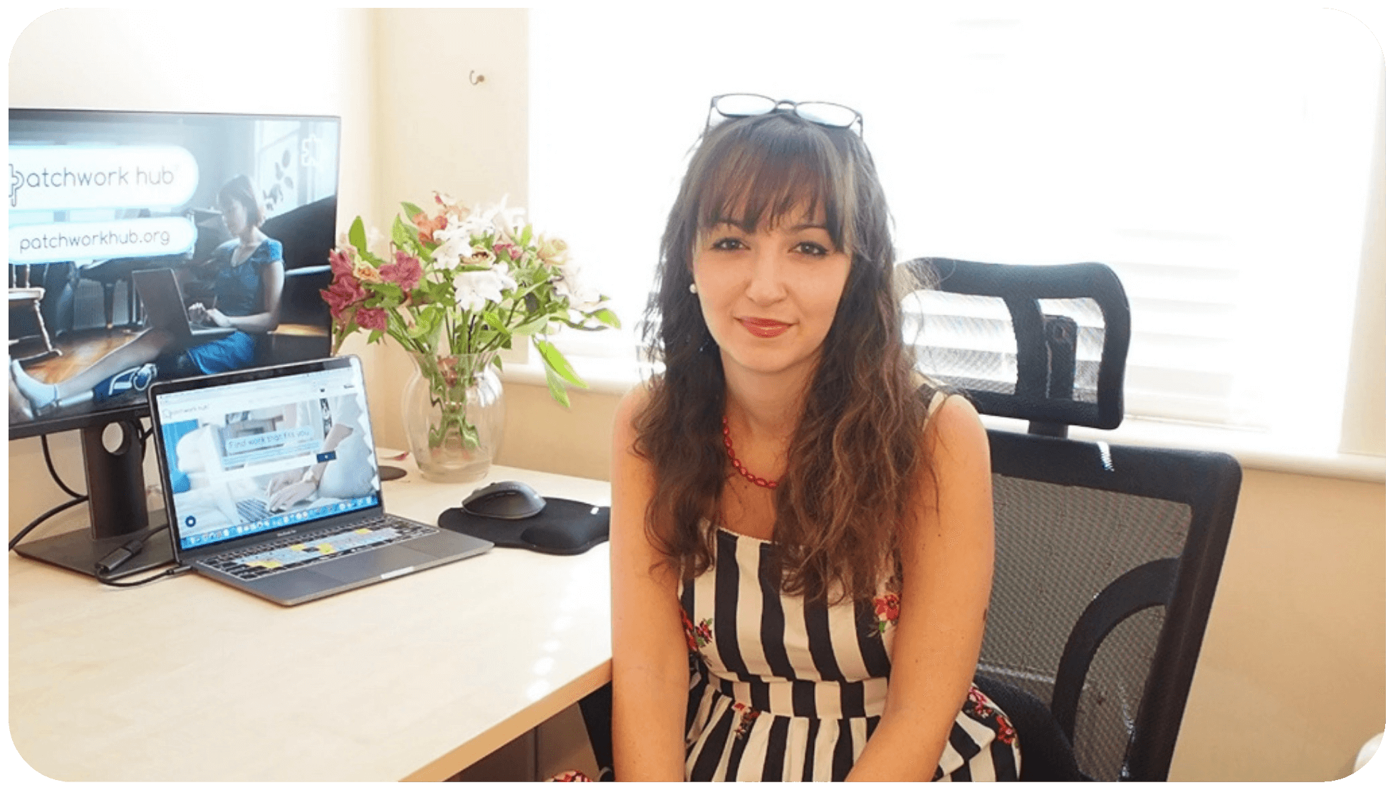 Beth smiling at camera in office with Patchwork Hub open on the monitor behind.