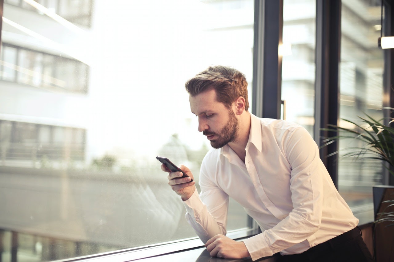 Man leaning against a window looking at a smartphone