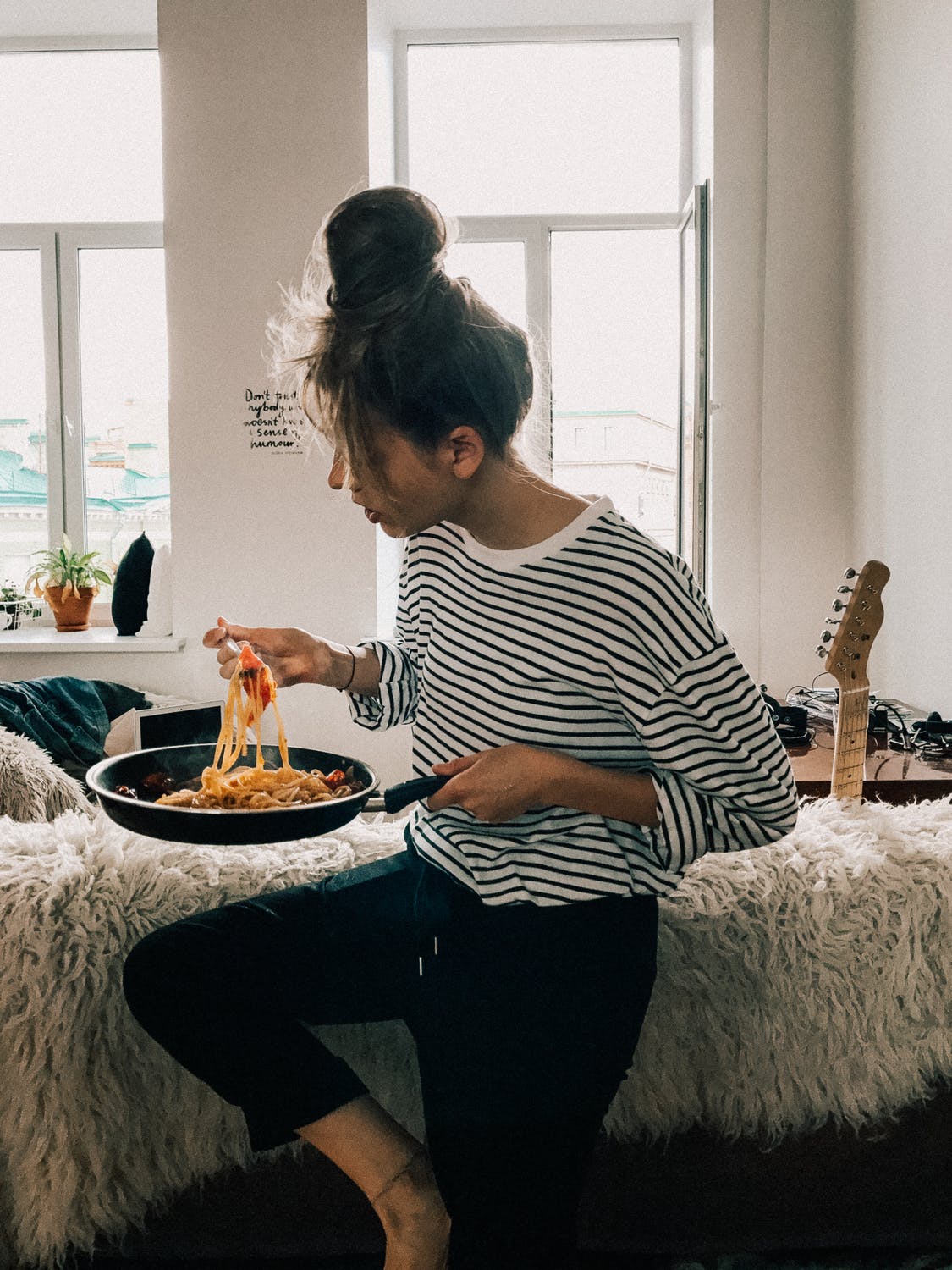 Girl in her college dorm casually eating pasta out of a pan