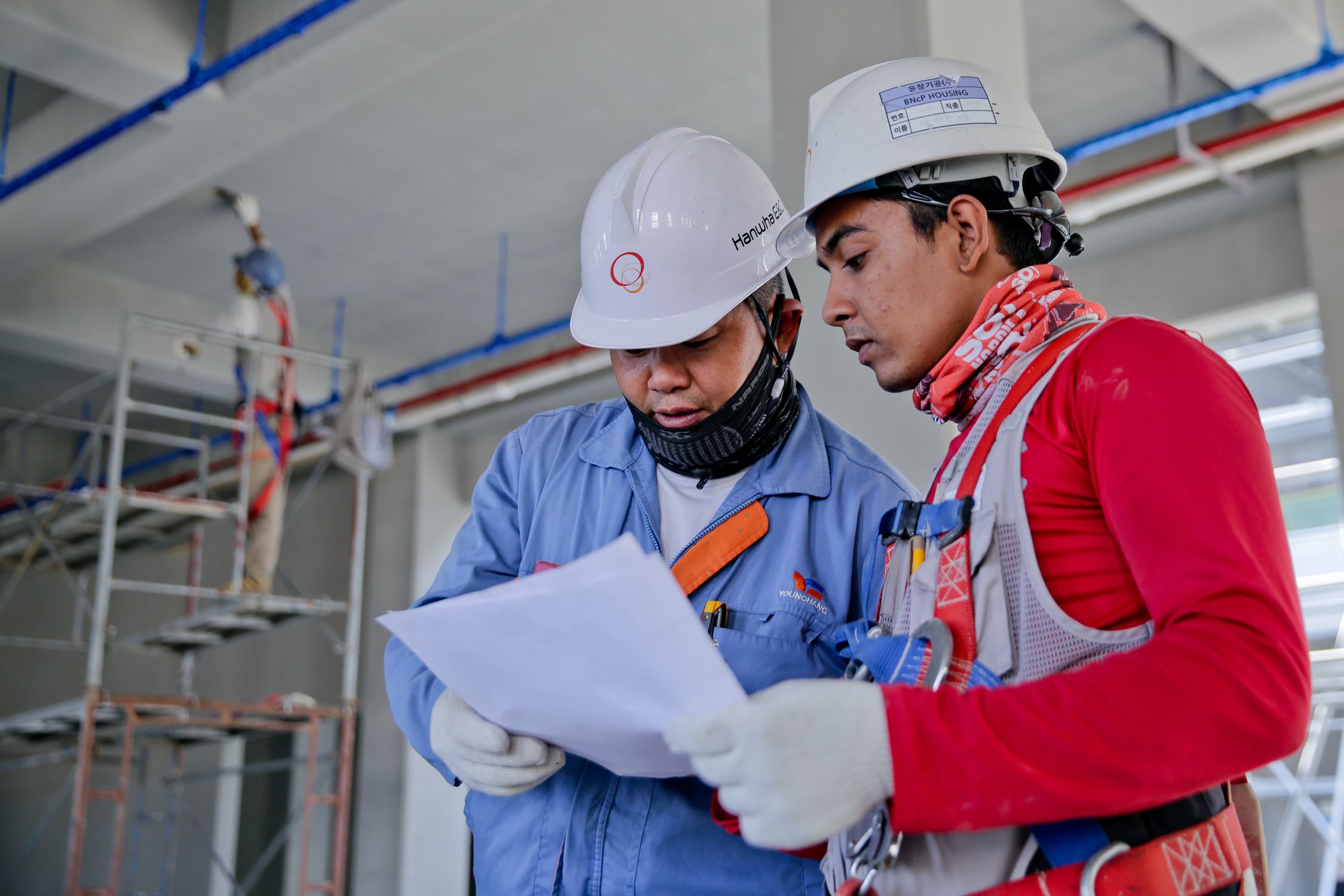 Two men in hard hats look over a blueprint together.