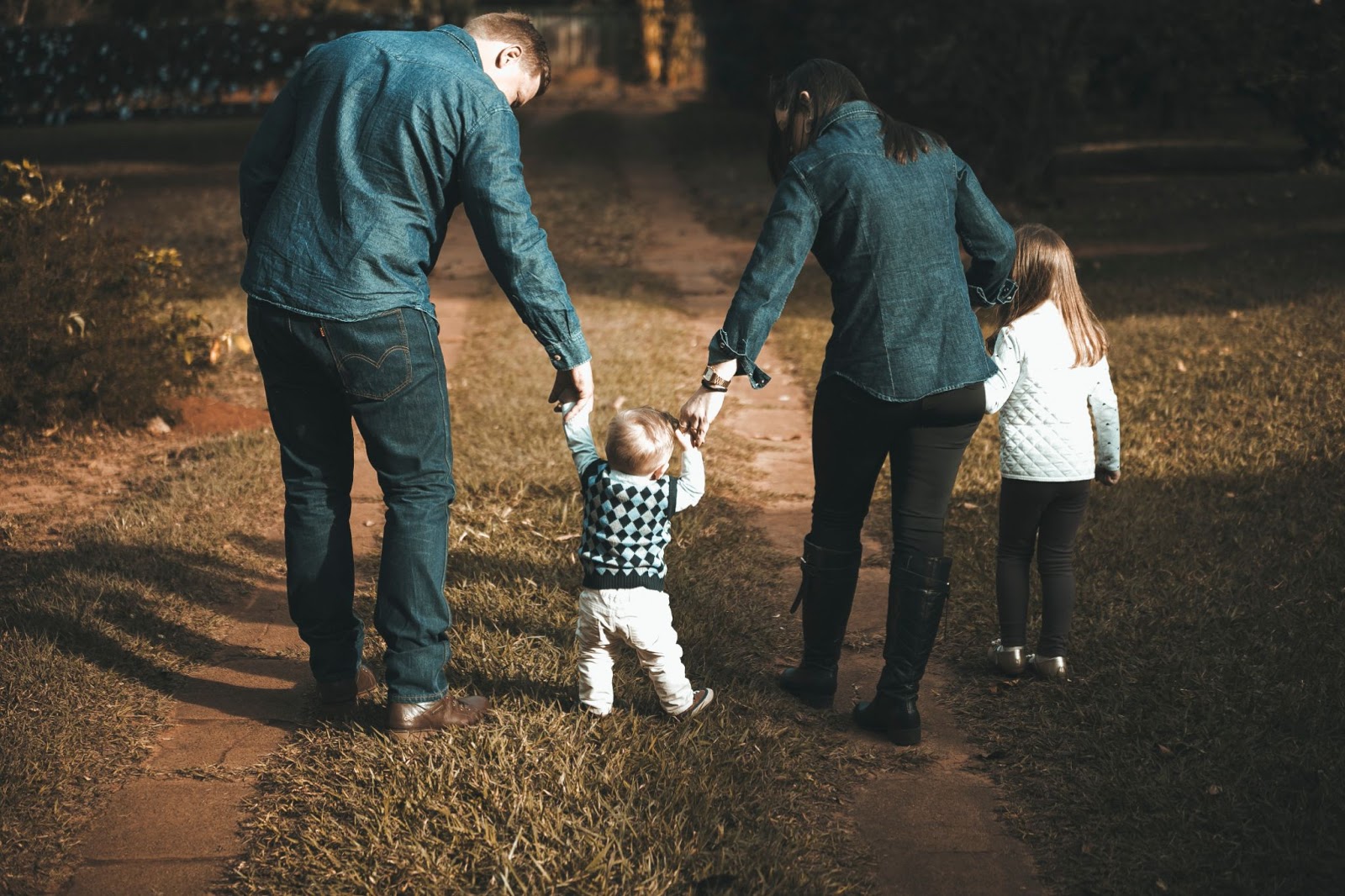 A mother and father hold their baby son and toddler daughters hand as they walk through a forest.