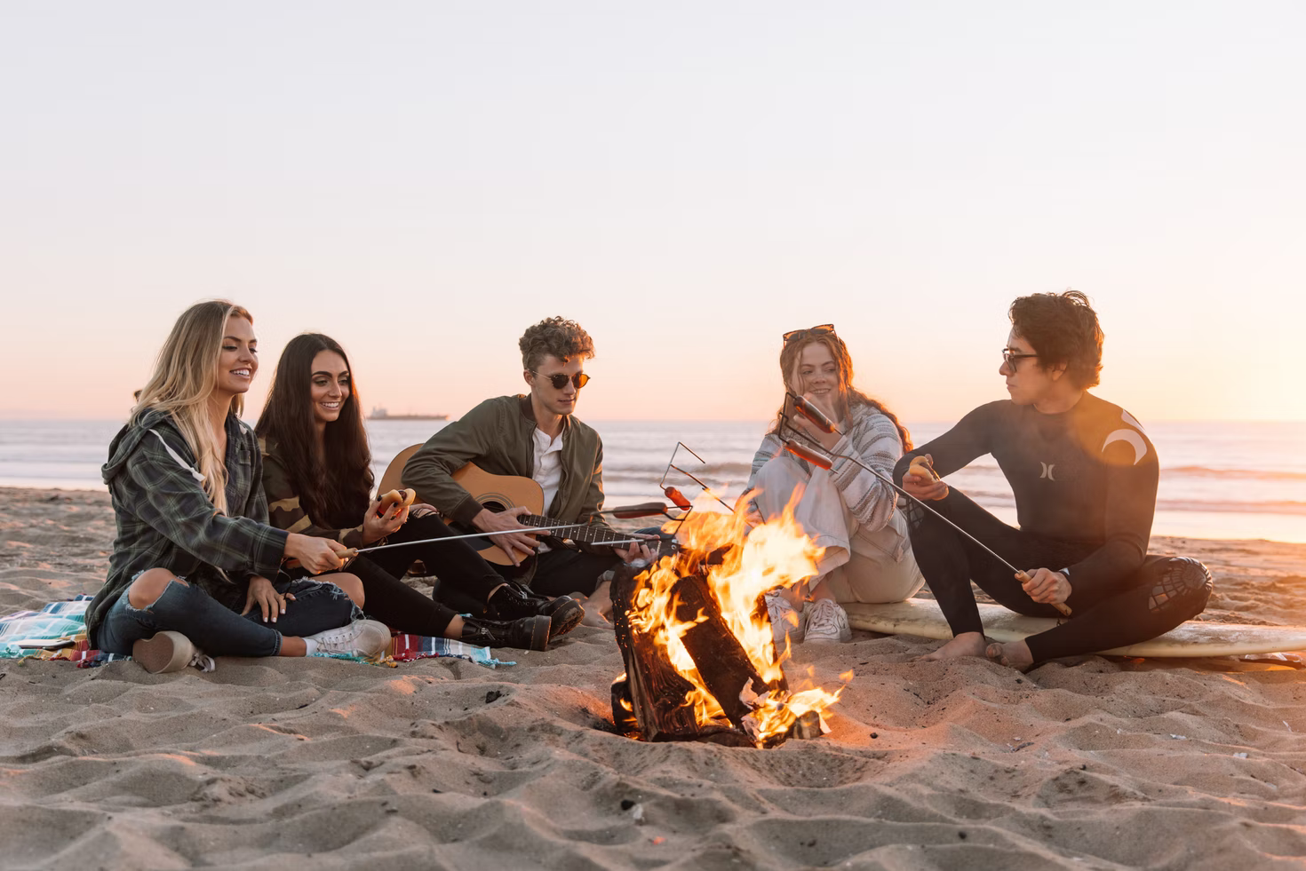People sitting on a beach with a campfire.