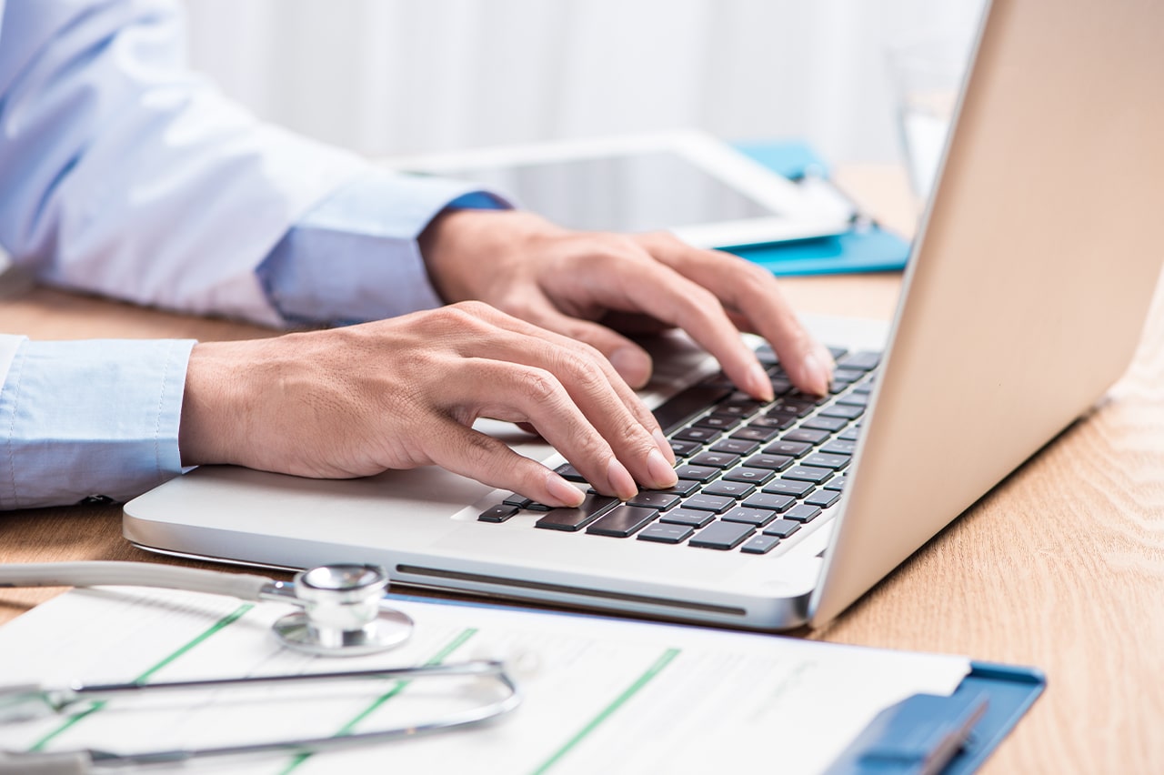 A physician types on a laptop