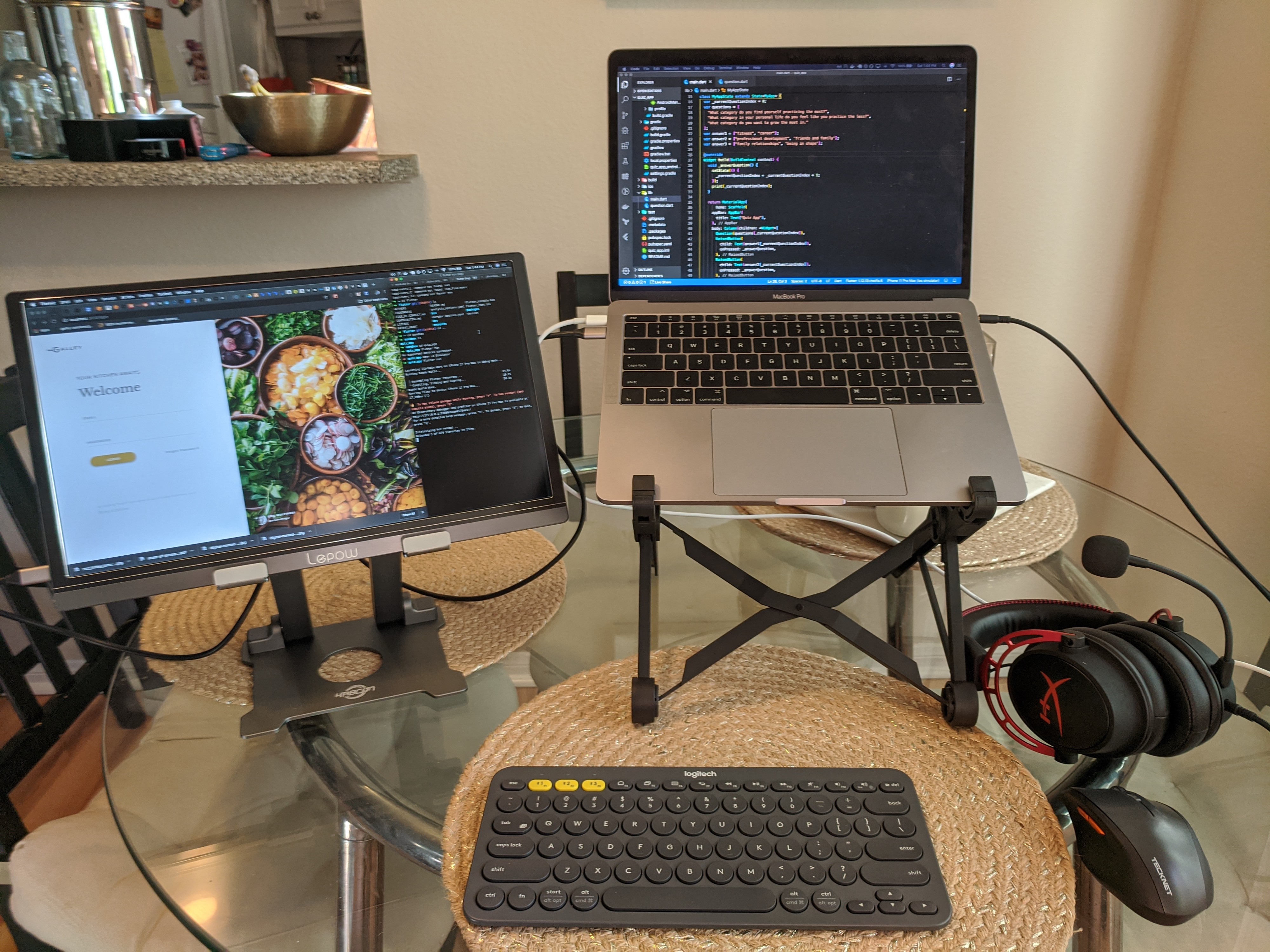 An external monitor on a tablet stand, a laptop on a laptop stand, a keyboard, mouse, and a set of headphones on a table.