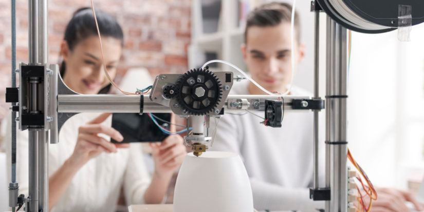 Two people behind a 3D printer