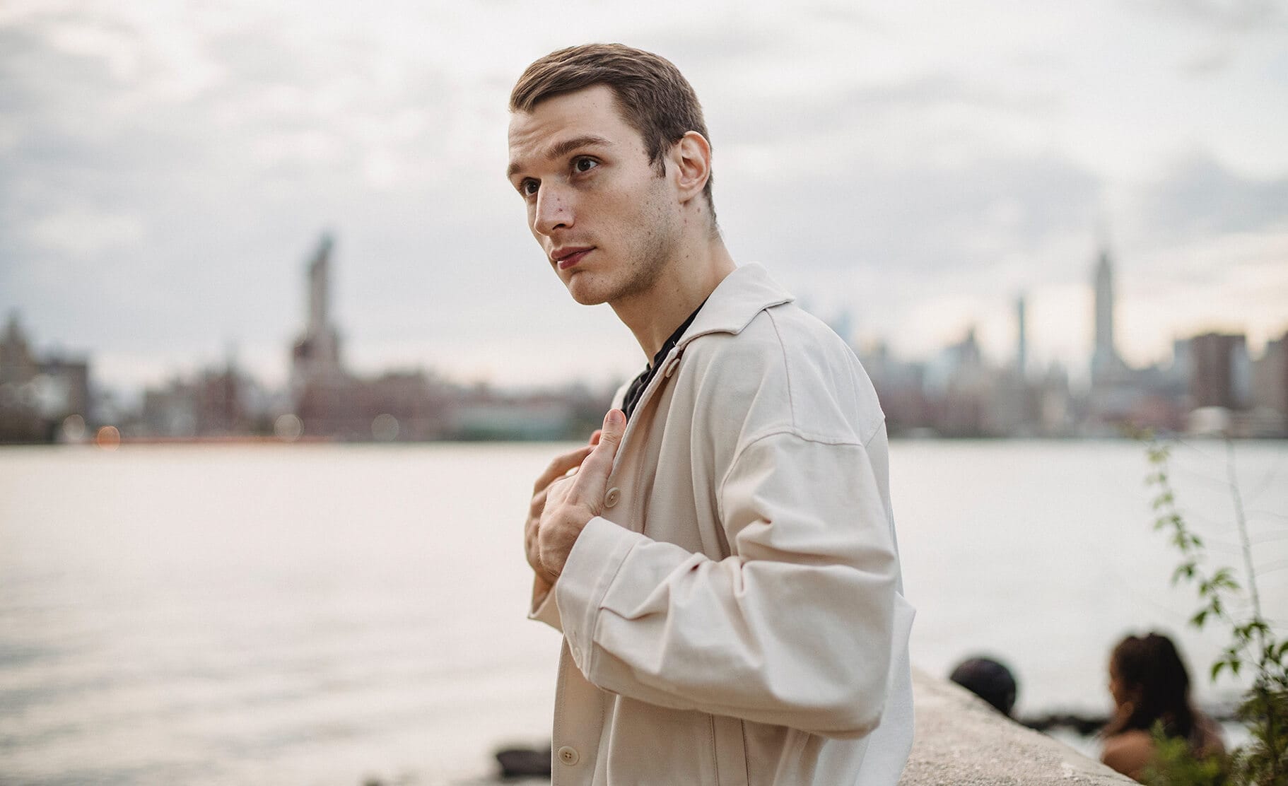 A man in a jacket next to a river placing his hands on his chest