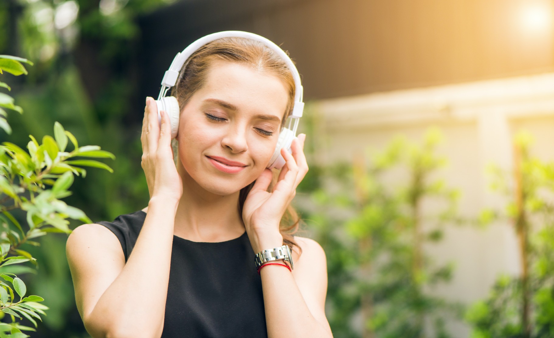 A grinning woman with over-ear headphones on cups her hands over her headphones