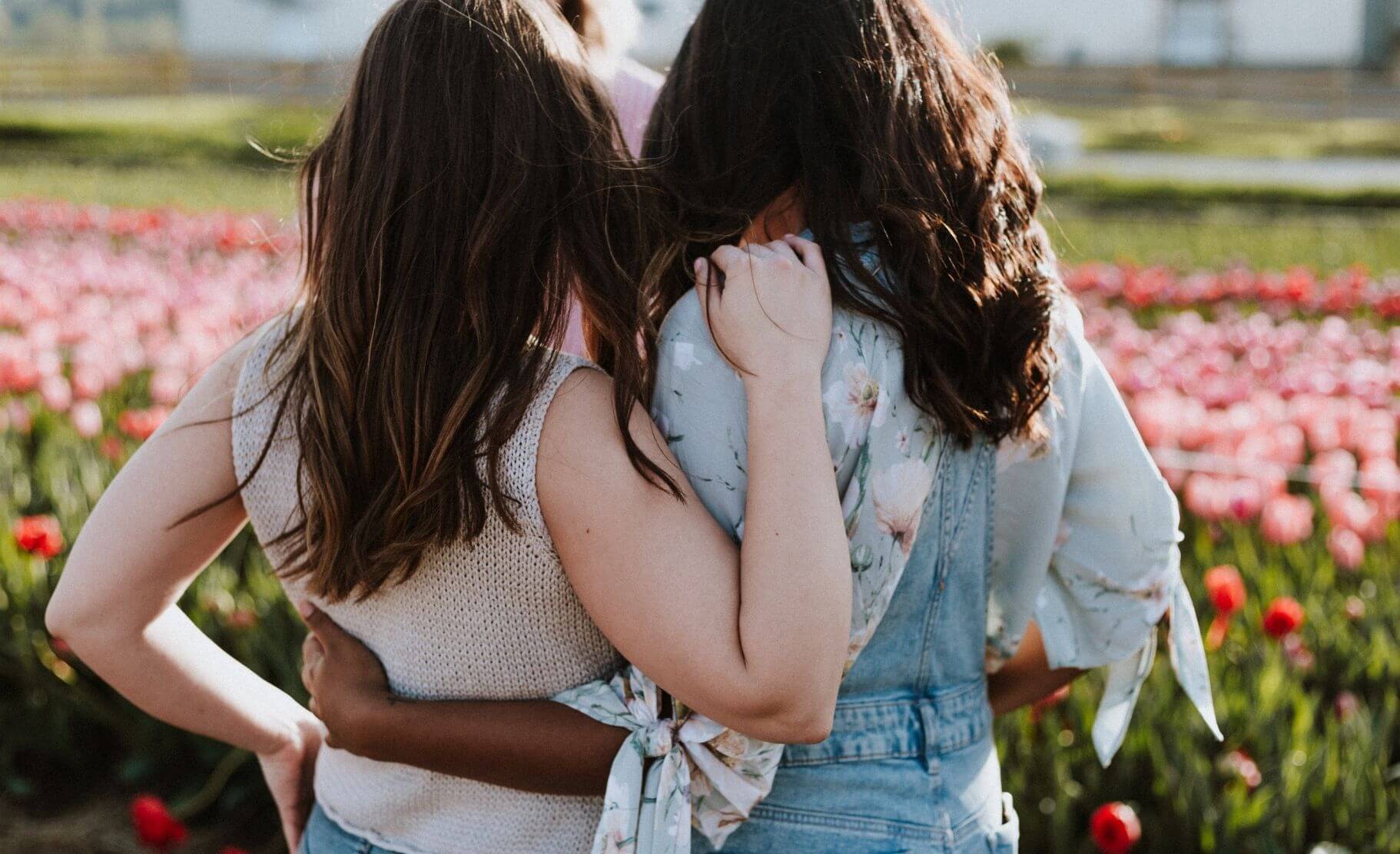 Two women share a friendly hug while looking at a field of flowers