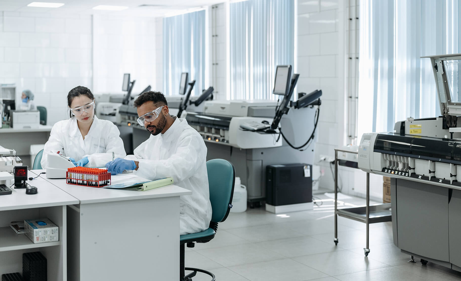 Two researchers in protective lab gear look at a vial