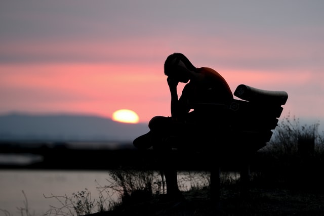 man sitting on park bench in front of lake, wondering "why am I so depressed?"