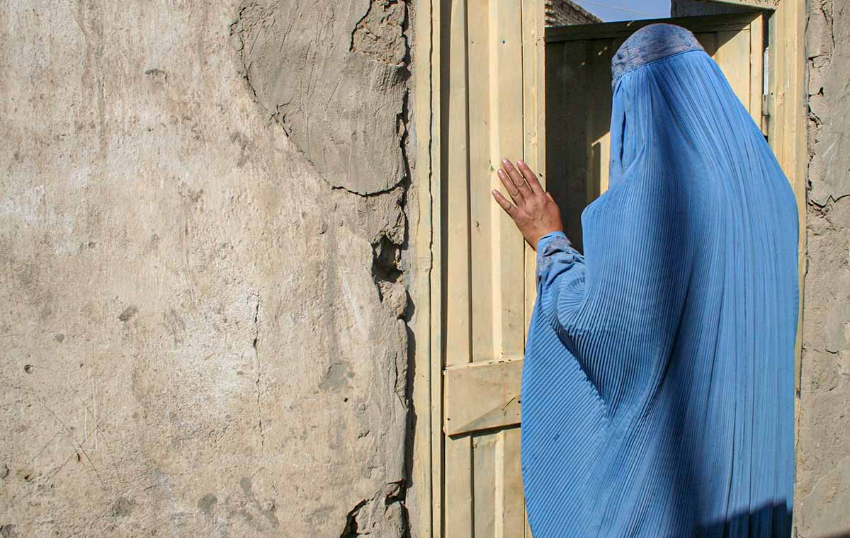 Afghan woman in blue burka standing by a door