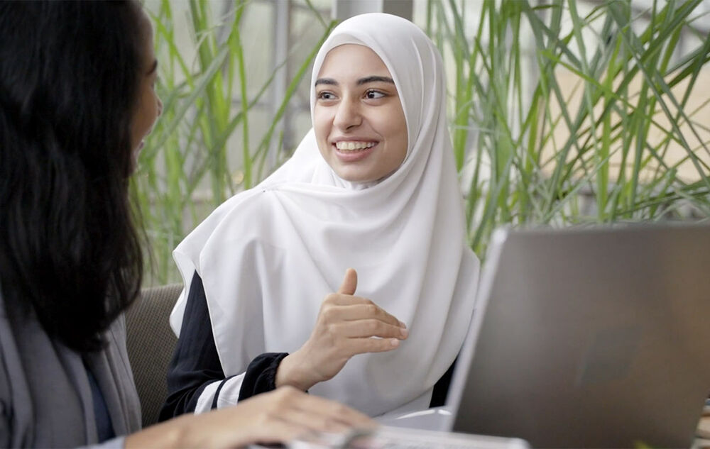 Woman in hijab by computer talking to a friend
