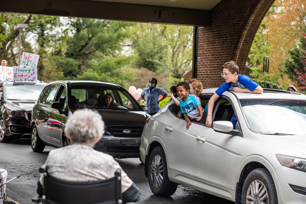 a stream of cars parade by a nursing home, greeting their loved ones through the windows.