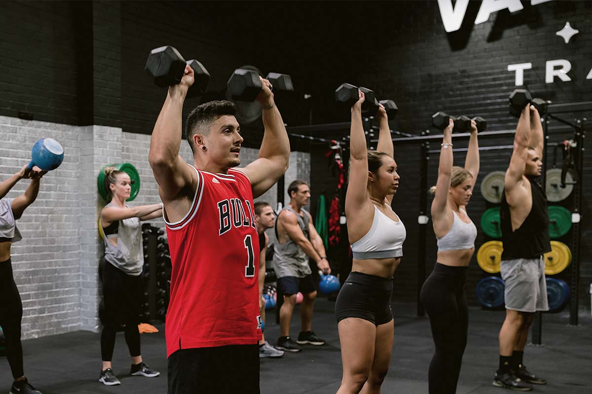 gym members lifting dumbbells above their heads