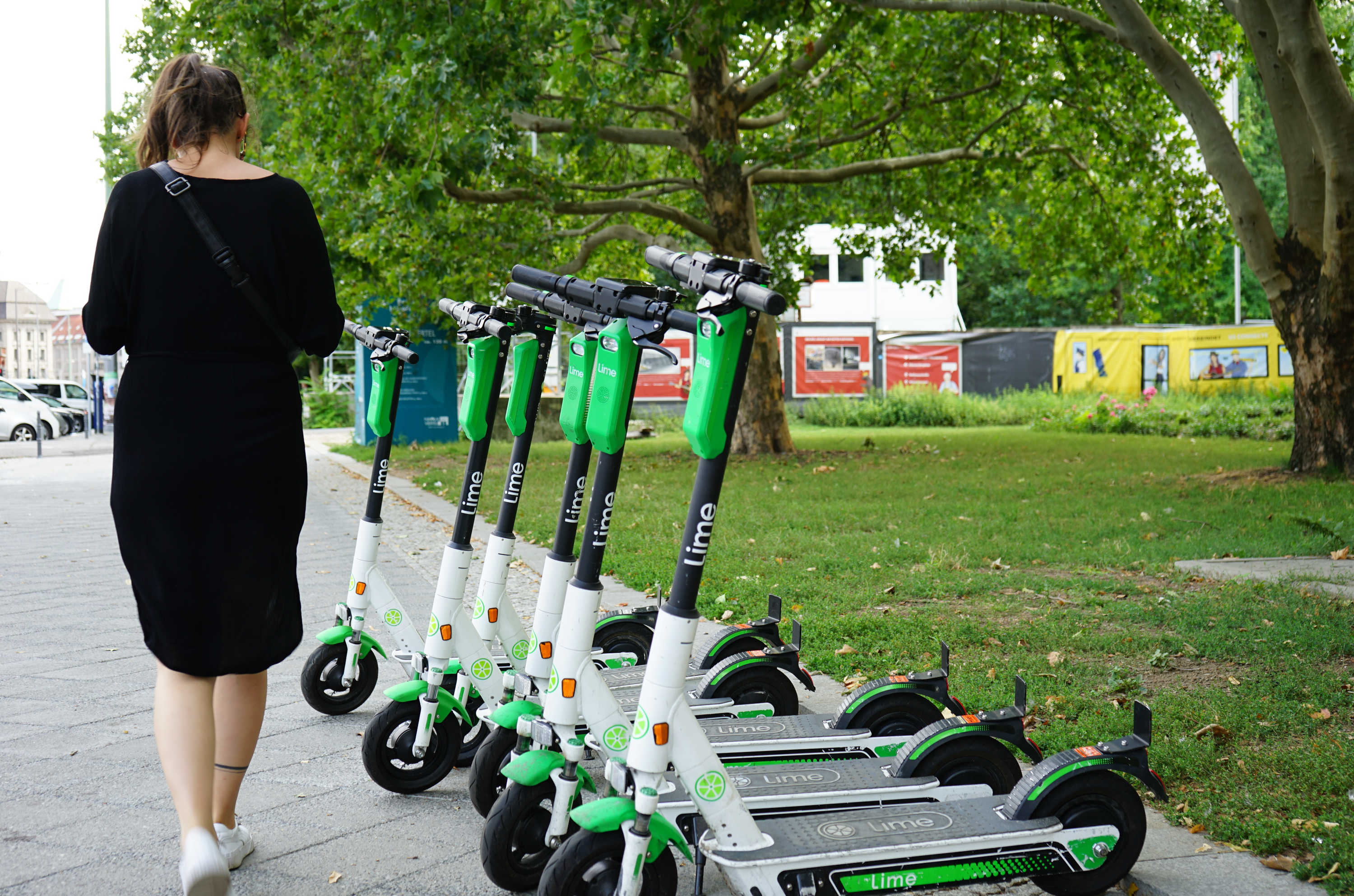 Una mujer pasa junto a una flota de e-scooters Lime sin muelle alineados en el pavimento