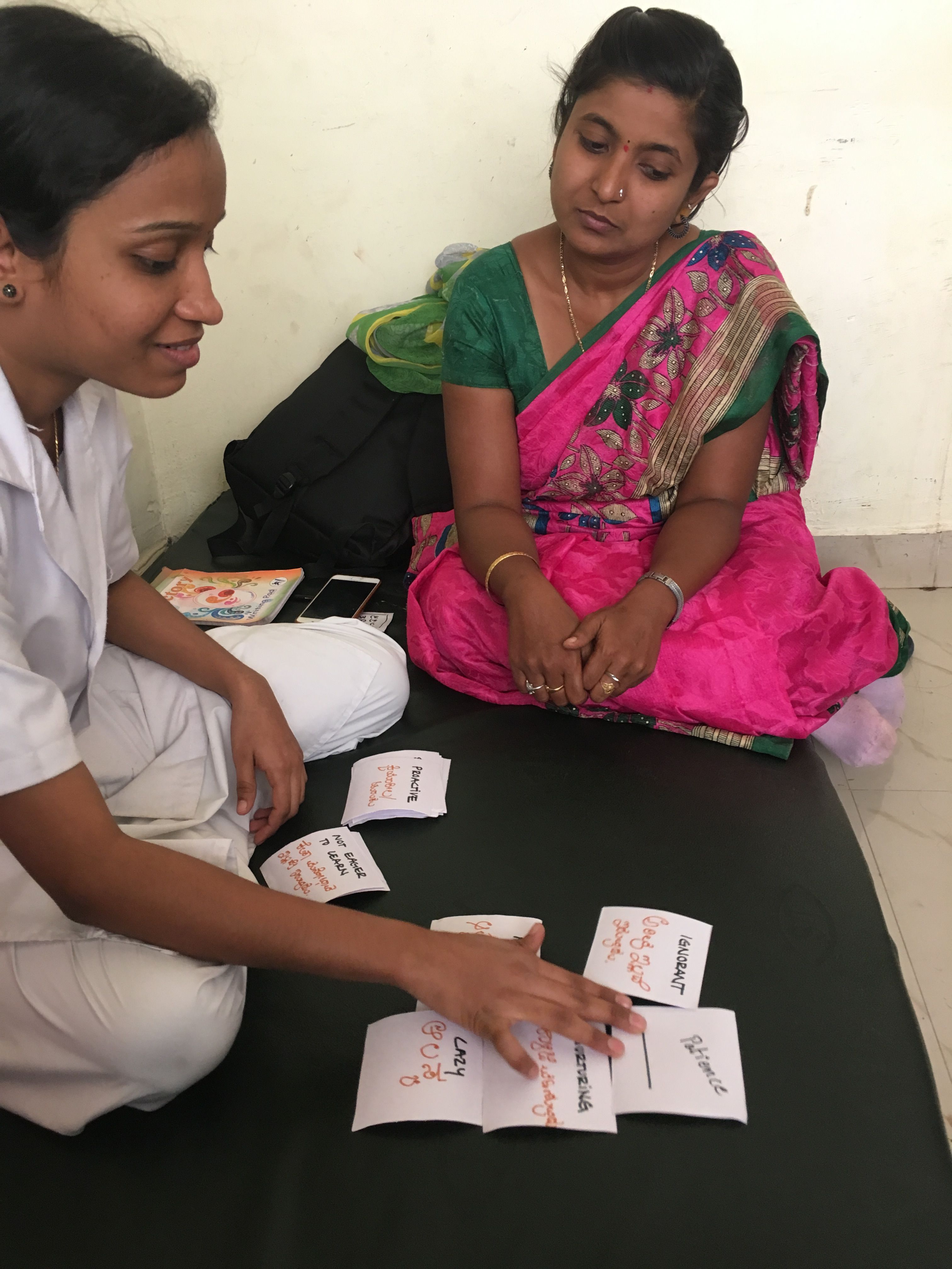 A woman uses paper cards as another woman looks on