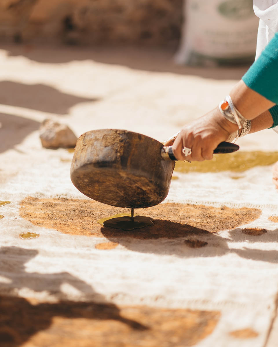 A woman weaver from the Anti Atlas pouring some henna paste on a wool weaving.