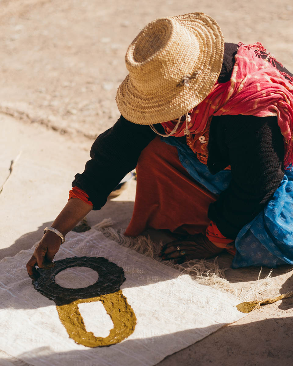 A woman weaver from the Anti Atlas paints a wool fabric with henna paste.