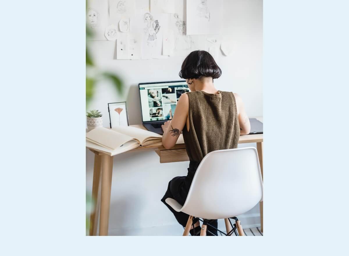 Eine junge Frau sitzt an einem Holztisch und recherchiert auf ihrem Laptop.