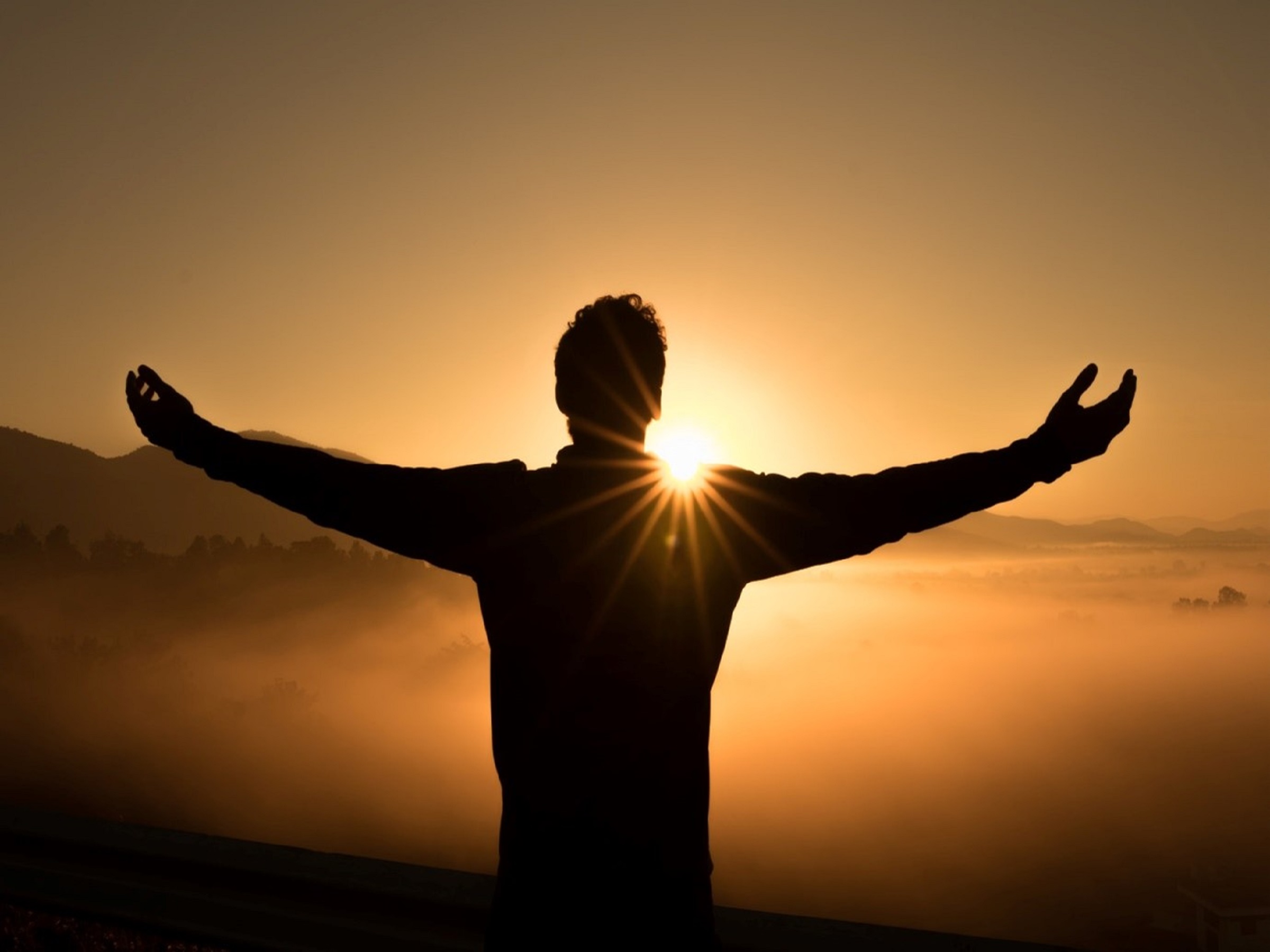 Silhouette of man with arms open looking out at sunset