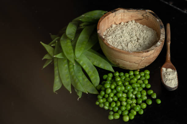 Pea protein powder and snap pea portrait Pea protein powder is pictured in a wooden bowl, and in a wooden spoon from a side view. Next to them is a pile of snow peas and snap peas. plant protein powder stock pictures, royalty-free photos & images