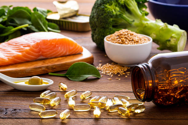 Fish oil capsules and diet rich in omega-3 Front view of many fish oil capsules spilling out from the bottle surrounded by an assortment of food rich in omega-3 such as salmon, flax seeds, broccoli, sardines, spinach, olives and olive oil. omega stock pictures, royalty-free photos & images
