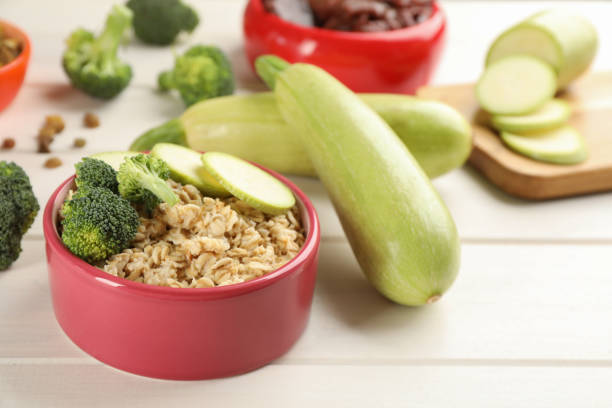Feeding bowl with oatmeal porridge and vegetables on white wooden table, closeup. Natural pet food Feeding bowl with oatmeal porridge and vegetables on white wooden table, closeup. Natural pet food dog zucchini stock pictures, royalty-free photos & images