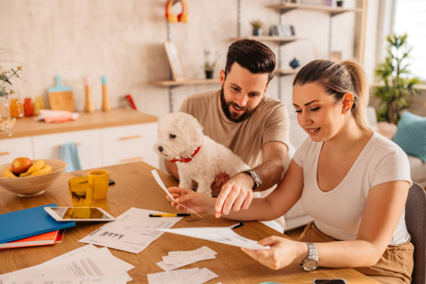 Couple checking their finances at home with their dog Young heterosexual couple sitting in their living room and checking their finances.  Man holding cute toy dog in his lap. pet insurance stock pictures, royalty-free photos & images