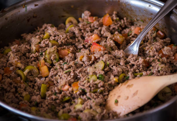Simple but delicious ground meat frying in pan! Close up shot using selective focus of a simple but appetizing homemade braising food, ground meat with chopped tomato and olive and onion, being prepared inside a pan with cutlery fresh dog food cooking in a pan stock pictures, royalty-free photos & images
