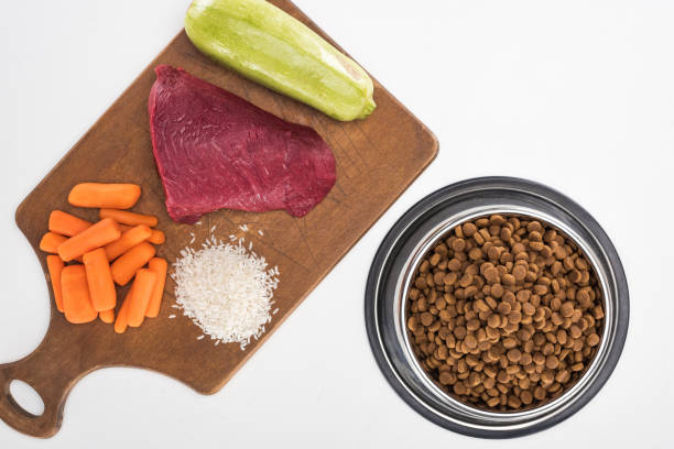 top view of dry pet food and raw meat, rice, carrot and zucchini on wooden cutting board isolated on white top view of dry pet food and raw meat, rice, carrot and zucchini on wooden cutting board isolated on white fresh dog food ingredeints stock pictures, royalty-free photos & images