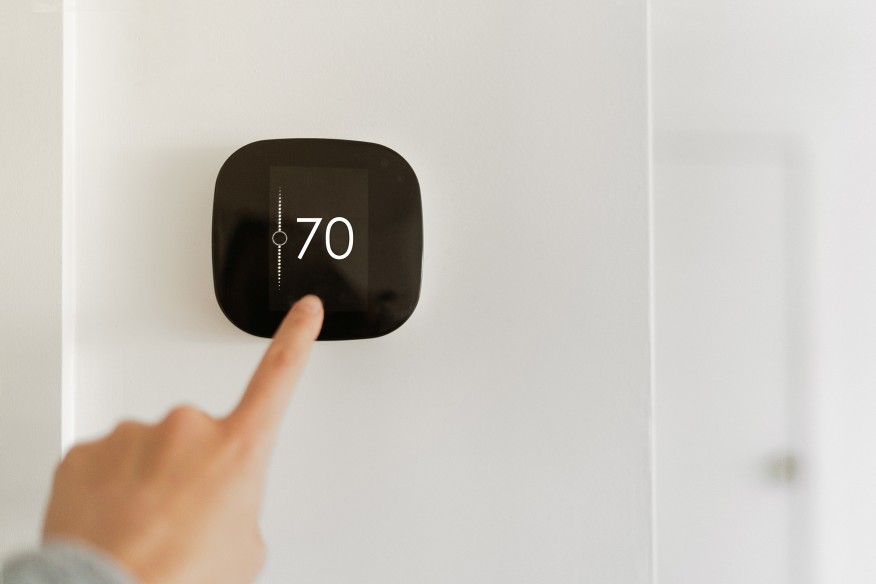Thermostat indoor smart home in house system for temperature. Winter heating energy efficient automation digital touchscreen wall hand touching device to adjust heating in living room. IoT domotics.