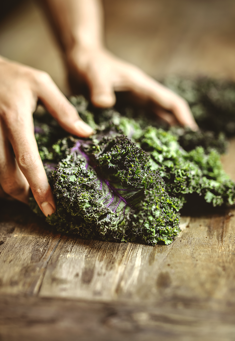 Hands pulling apart raw leafy kale on a wooden cutting board.