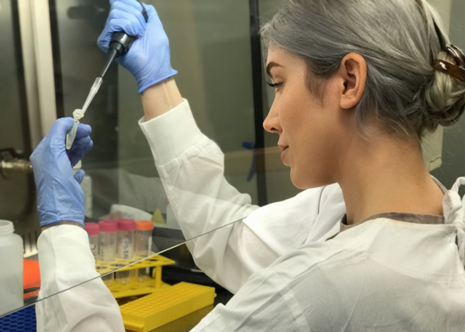 Morgan Freney at work in the lab in her white coat using a pipette to put solution into a tube.