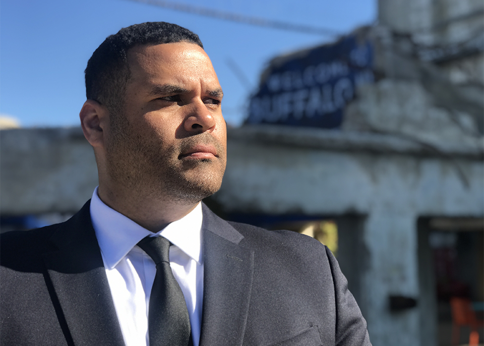 Albert Sye in a suit looking off to the side with a cityscape behind him.