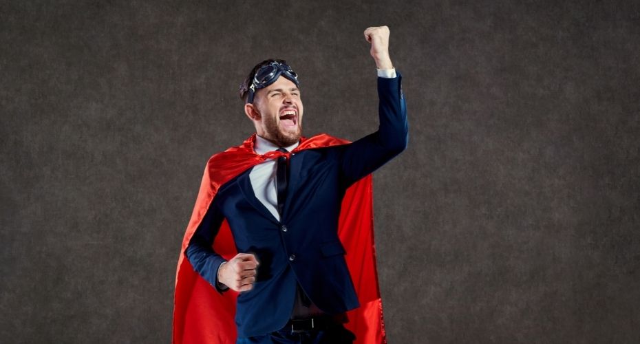 A lawyer wearing a suit, a superhero cape, and goggles raises their fist in the air in a successful cheer.