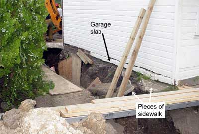 Pieces of sidewalk in the collapsed area and the garage slab foundation separated from the foundation. Notice, there is no protection in place to avoid the cave-in hazard.