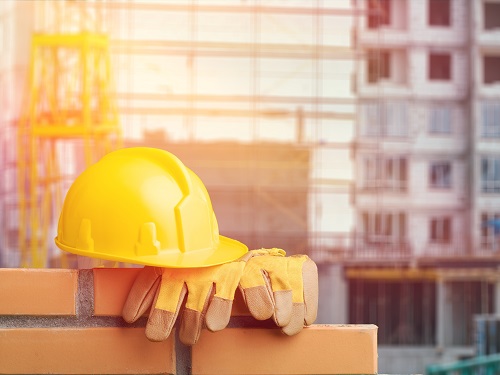 Hard Hat and Work Gloves Resting on Bricks with Construction Site in Background