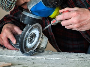 Worker Wearing Respirator is Fixing a Portable Grinder