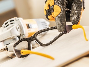 Construction Worker's Hand Reaching for Safety Glasses Before Using Grinder