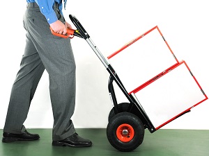 Worker in professional clothing pushing a handcart with two boxes on it.