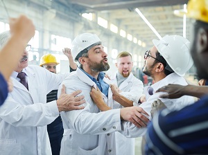 Two workers in an industrial setting physically fighting with each other.