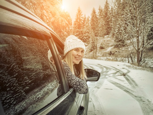 Woman leaning out of car window on snowy road.