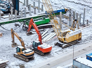 Heavy equipment and excavators on a construction site during winter with visible snow on the ground.