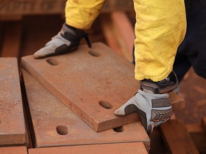 Worker lifting heavy work materials while wearing work gloves.
