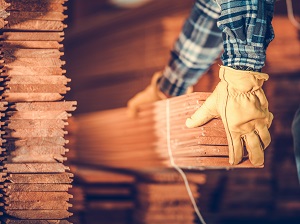 While wearing work gloves, a worker is removing a long bundle of wood from a pile.