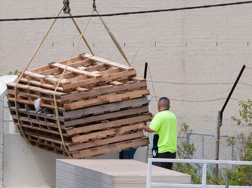 Construction workers moving pallets with a crane demonstrating a caught-in risk.
