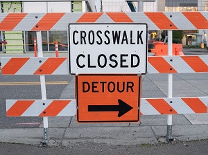 Orange and white street barricade with two signs that say Detour and Crosswalk Closed.
