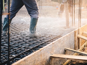 Worker standing on rebar pouring cement into formwork.