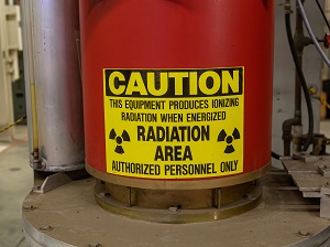 Industrial equipment with a large yellow caution sign that says, "Caution, This equipment produces ionizing radiation when energized, Radiation Area, Authorized Personnel Only."