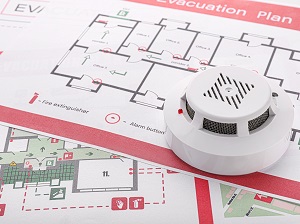 A smoke detector sitting on top of printed evacuation building plans as an image that depicts fire safety awareness.
